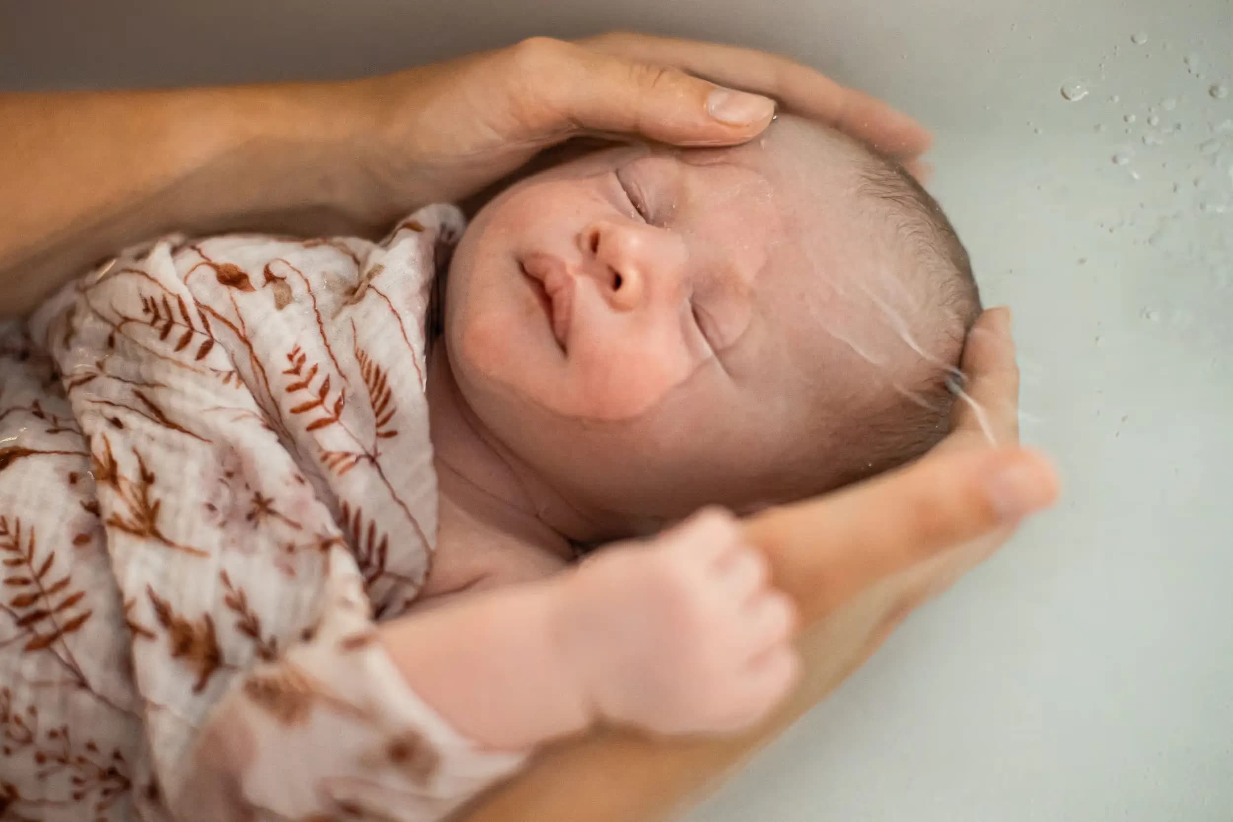 Un bébé enveloppé et soutenu délicatement pendant son bain